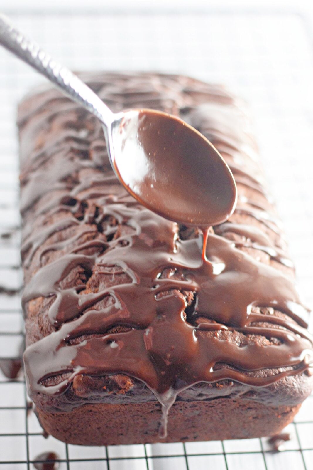 Spooning chocolate fudge frosting over the loaf on a wire rack