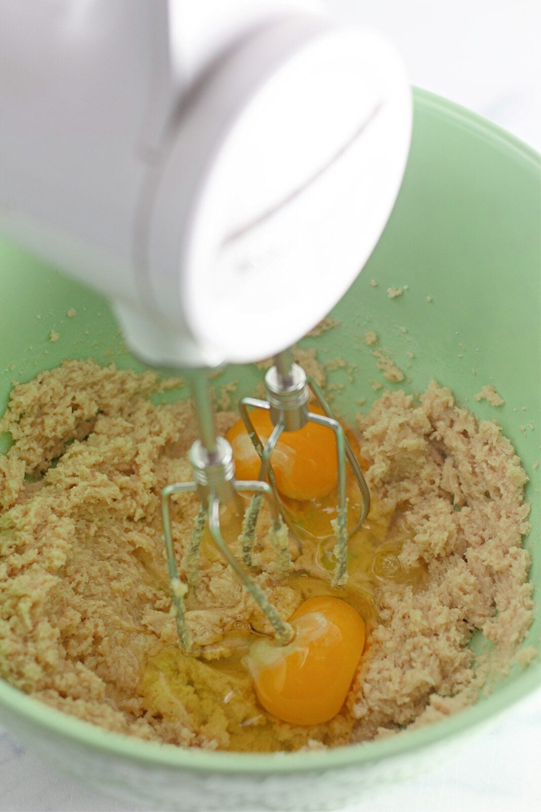 Eggs and mashed bananas added to creamed butter and sugars in a green bowl