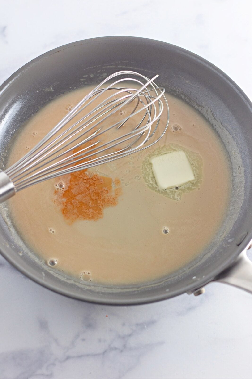 Heavy cream, brown sugar, butter, and vanilla heating in a skillet with a whisk