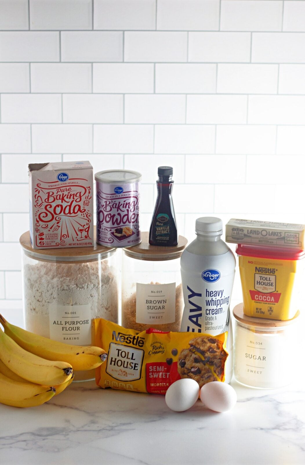 Chocolate banana bread ingredients including ripe bananas, flour, cocoa powder, sugars, eggs, butter, chocolate chips, and heavy cream