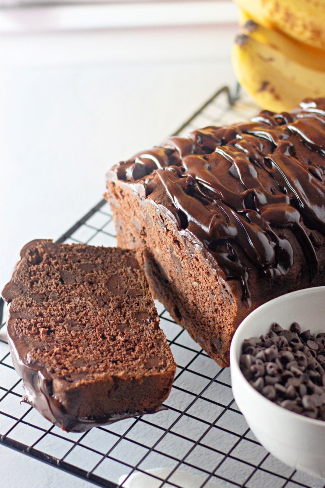 Sliced chocolate banana bread showing moist crumb next to a bowl of chocolate chips
