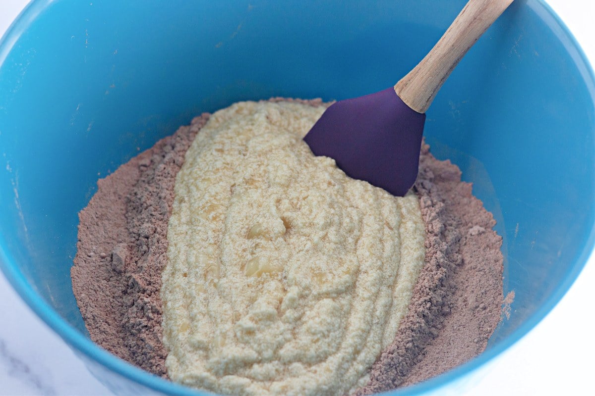 Wet banana mixture poured into the cocoa flour mixture in a blue bowl