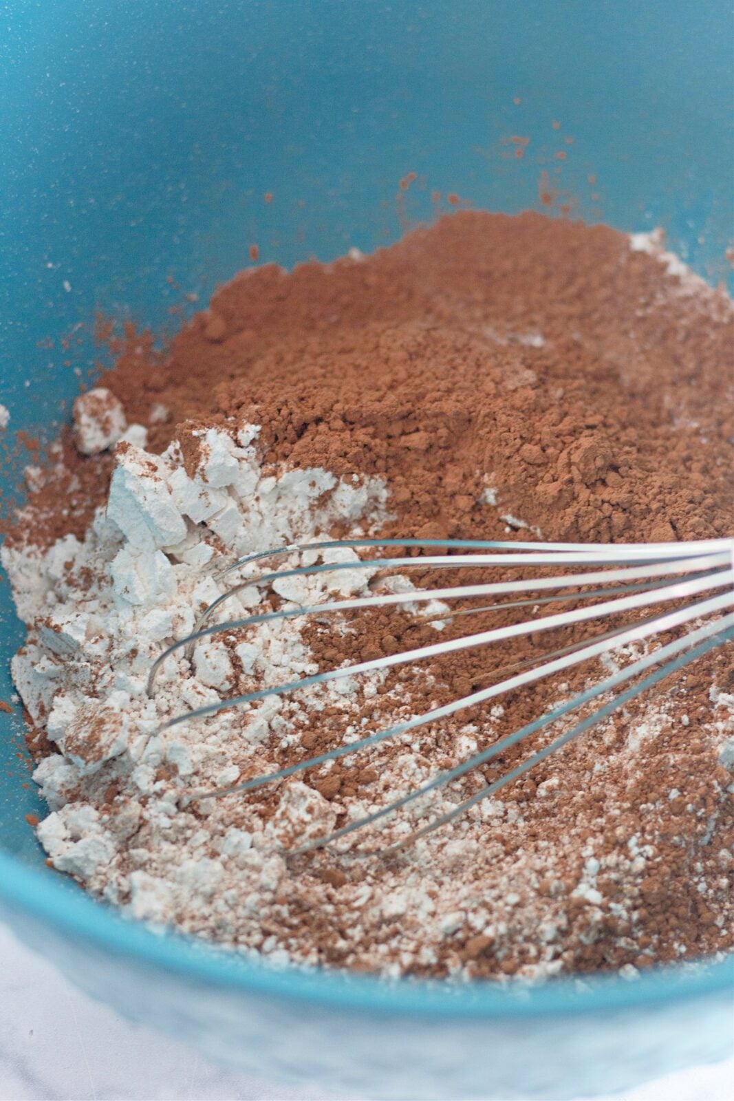Whisking flour, cocoa powder, baking soda, and baking powder in a blue bowl