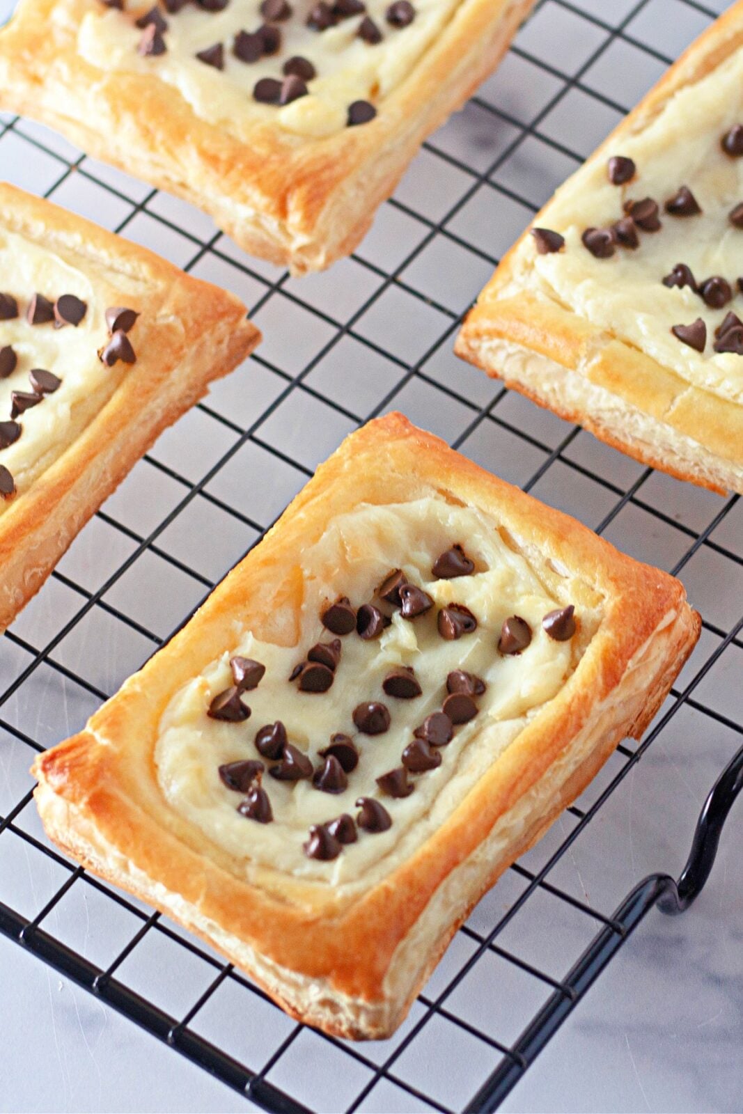 Golden chocolate chip cream cheese danishes cooling on a black wire rack