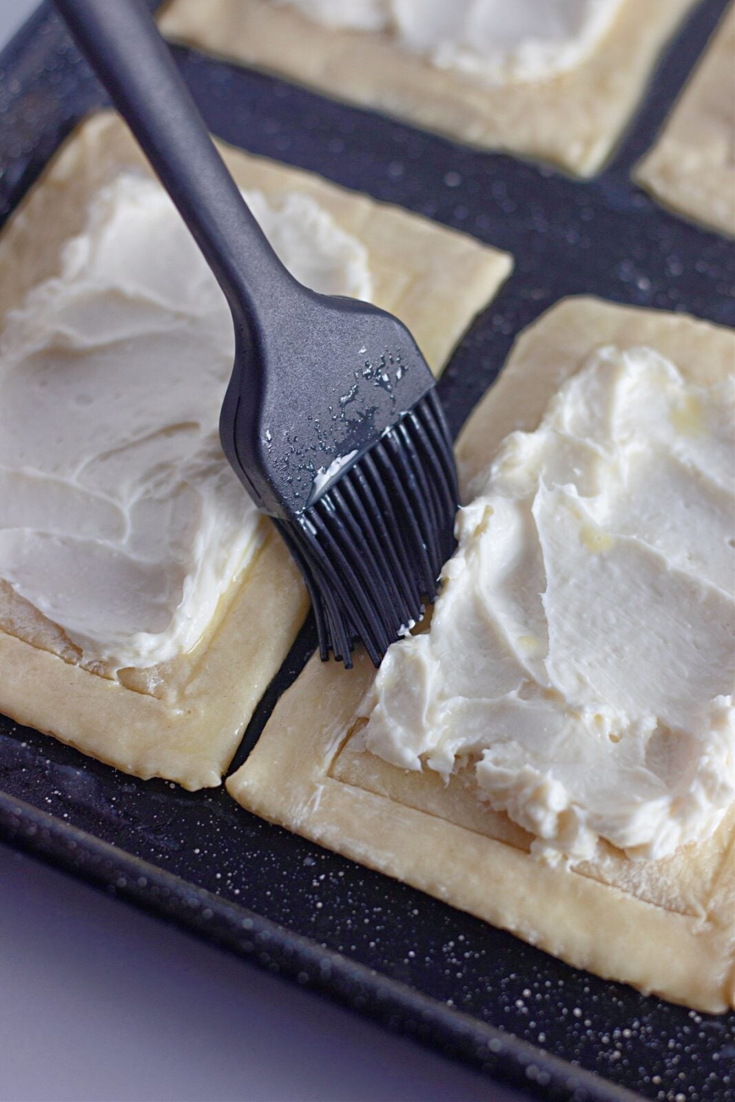 Brushing egg wash onto the pastry border with a black pastry brush