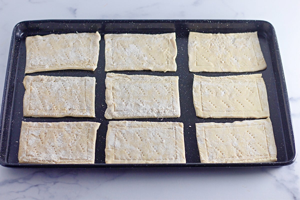 Puff pastry rectangles arranged on a large dark baking sheet