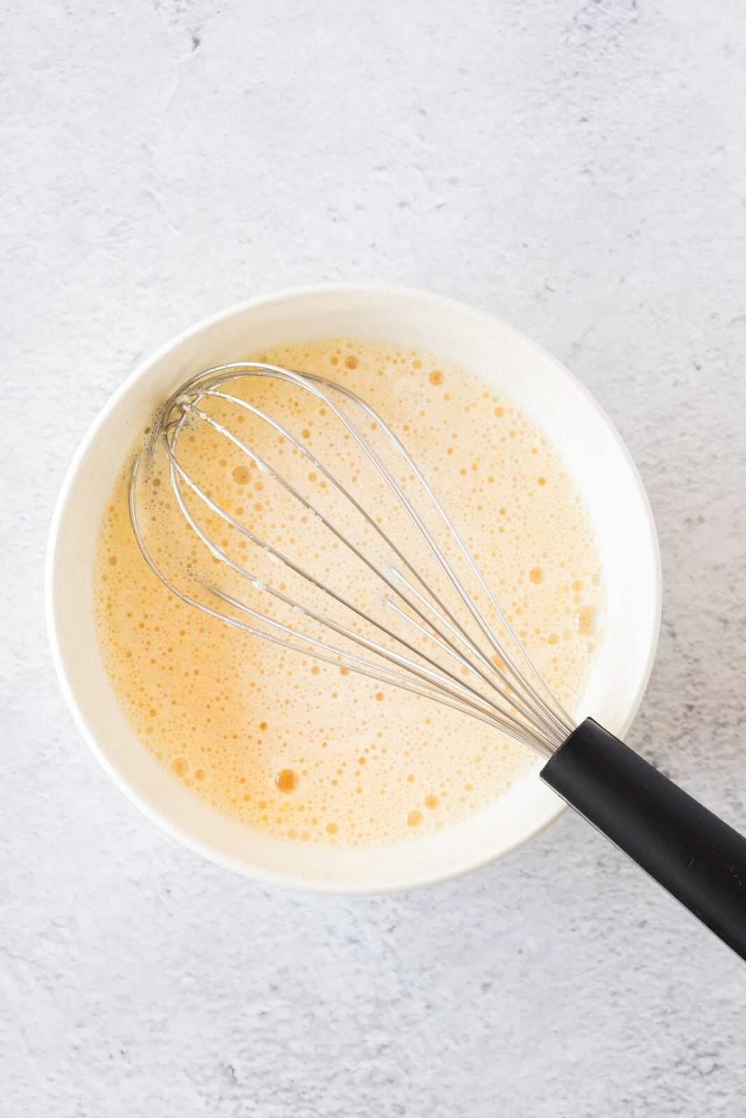 Eggs and sugar beaten until foamy in a white bowl with a whisk