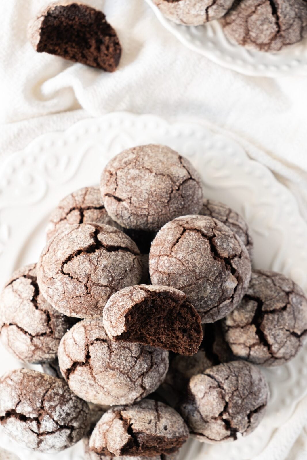 Pile of chocolate snowball cookies with one broken open on a white plate