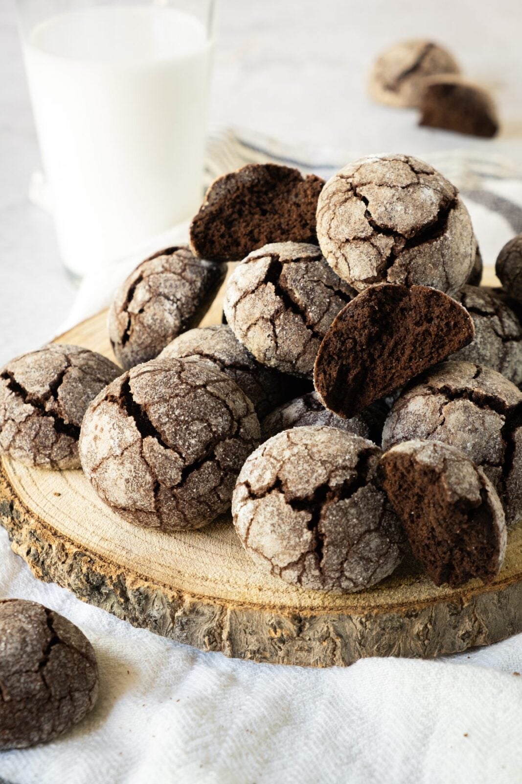 Chocolate snowball cookies stacked on a rustic wood slab with milk