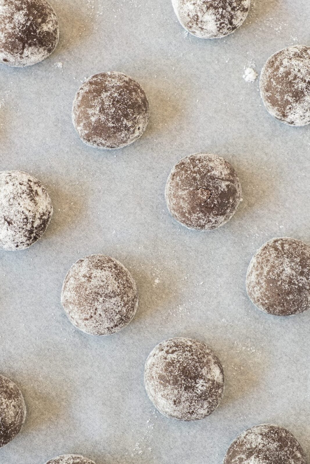 Chocolate dough balls rolled in powdered sugar on a parchment lined tray