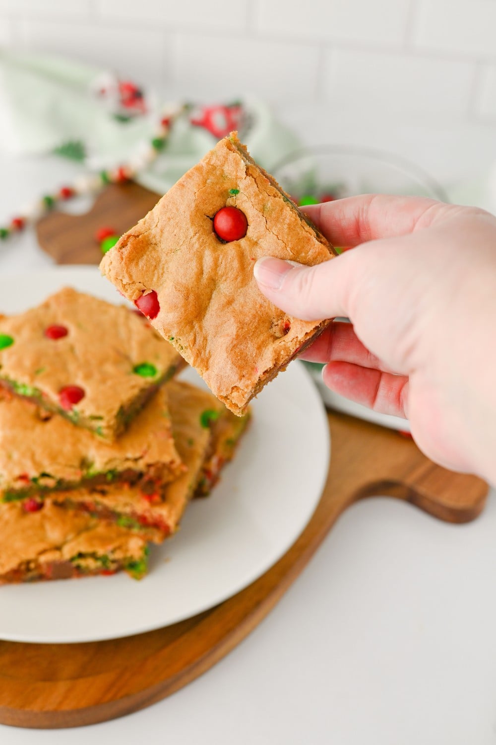 Hand holding a chewy Christmas cookie bar with a red M&M
