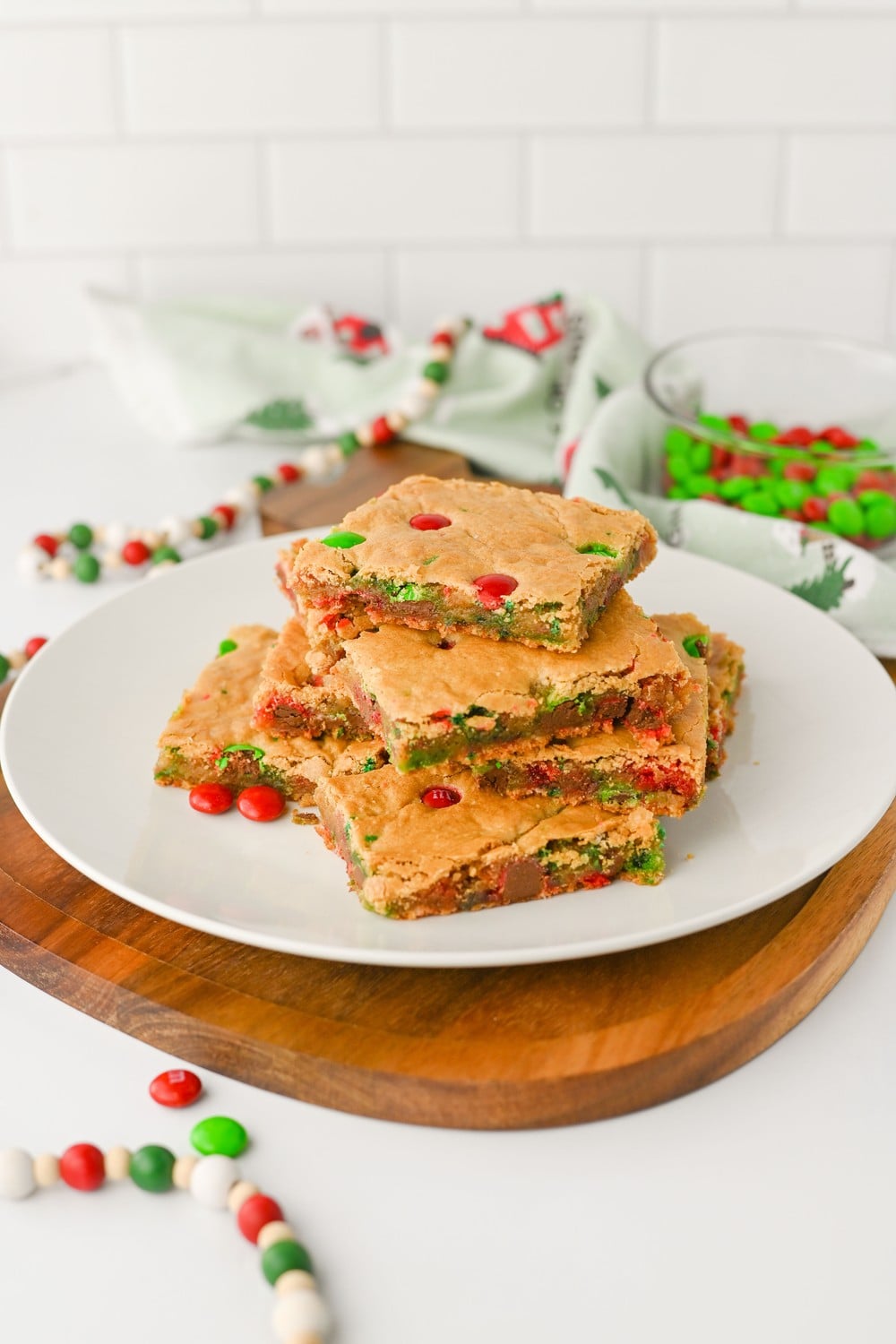 Stack of chewy Christmas cookie bars with red and green M&Ms on a white plate