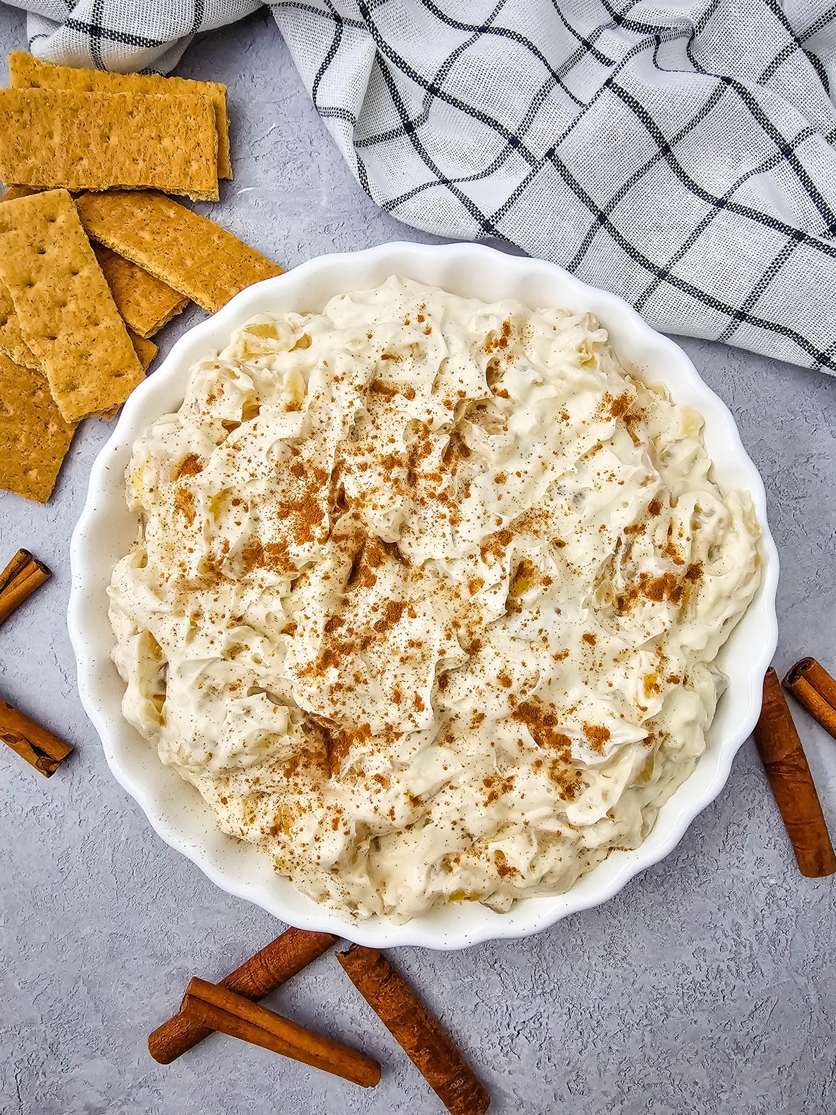 Creamy apple pie dip in a white fluted dish with graham crackers and cinnamon sticks