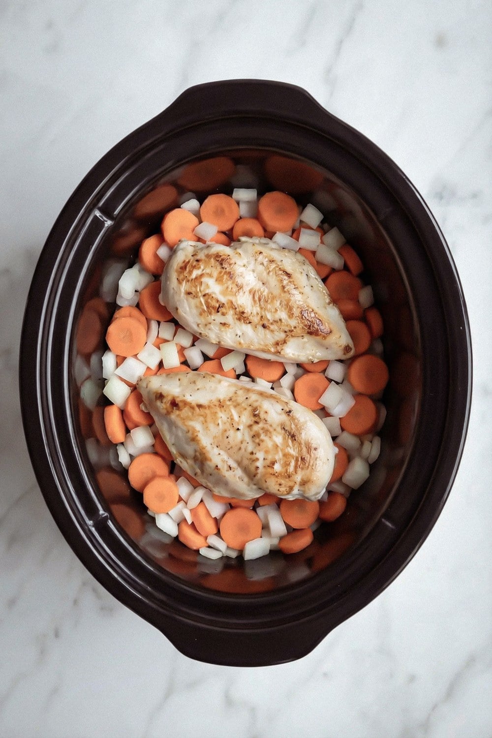 Chicken breasts on top of carrots and onion in a slow cooker