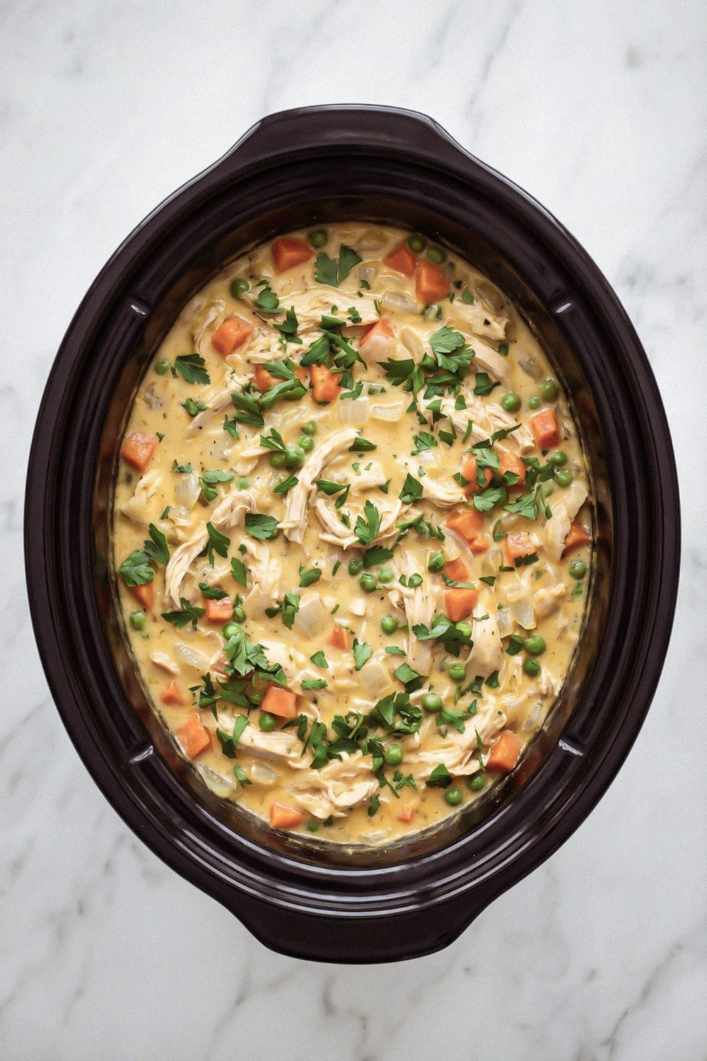 Finished crockpot chicken casserole with peas, carrots, and parsley in the slow cooker