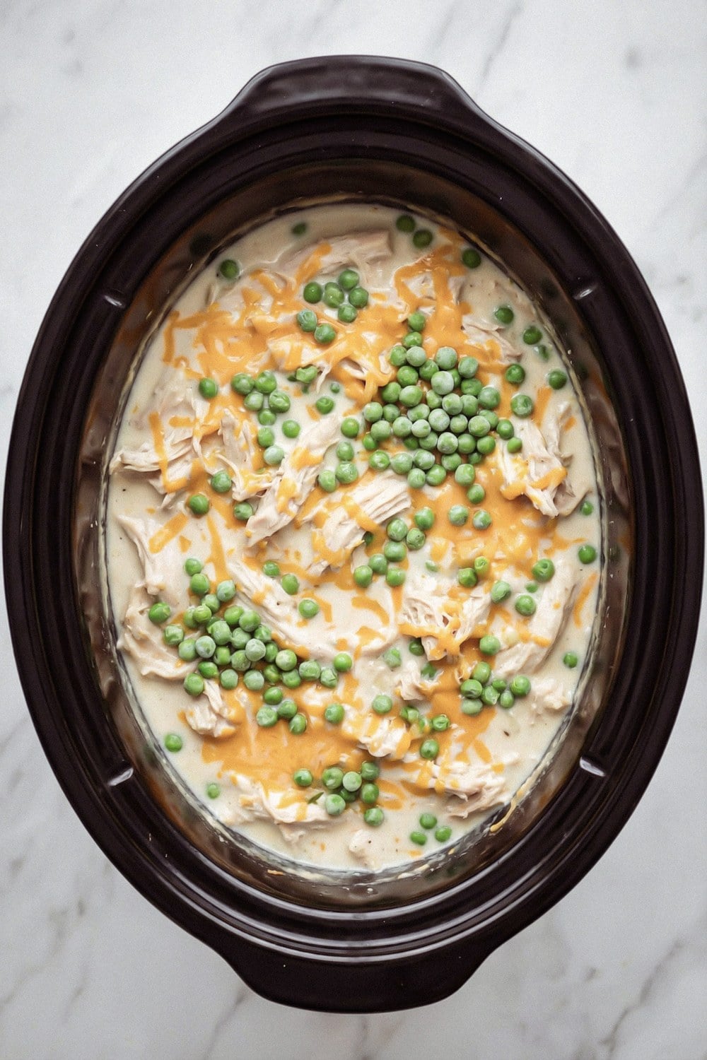 Peas and shredded cheddar added to the chicken in the slow cooker