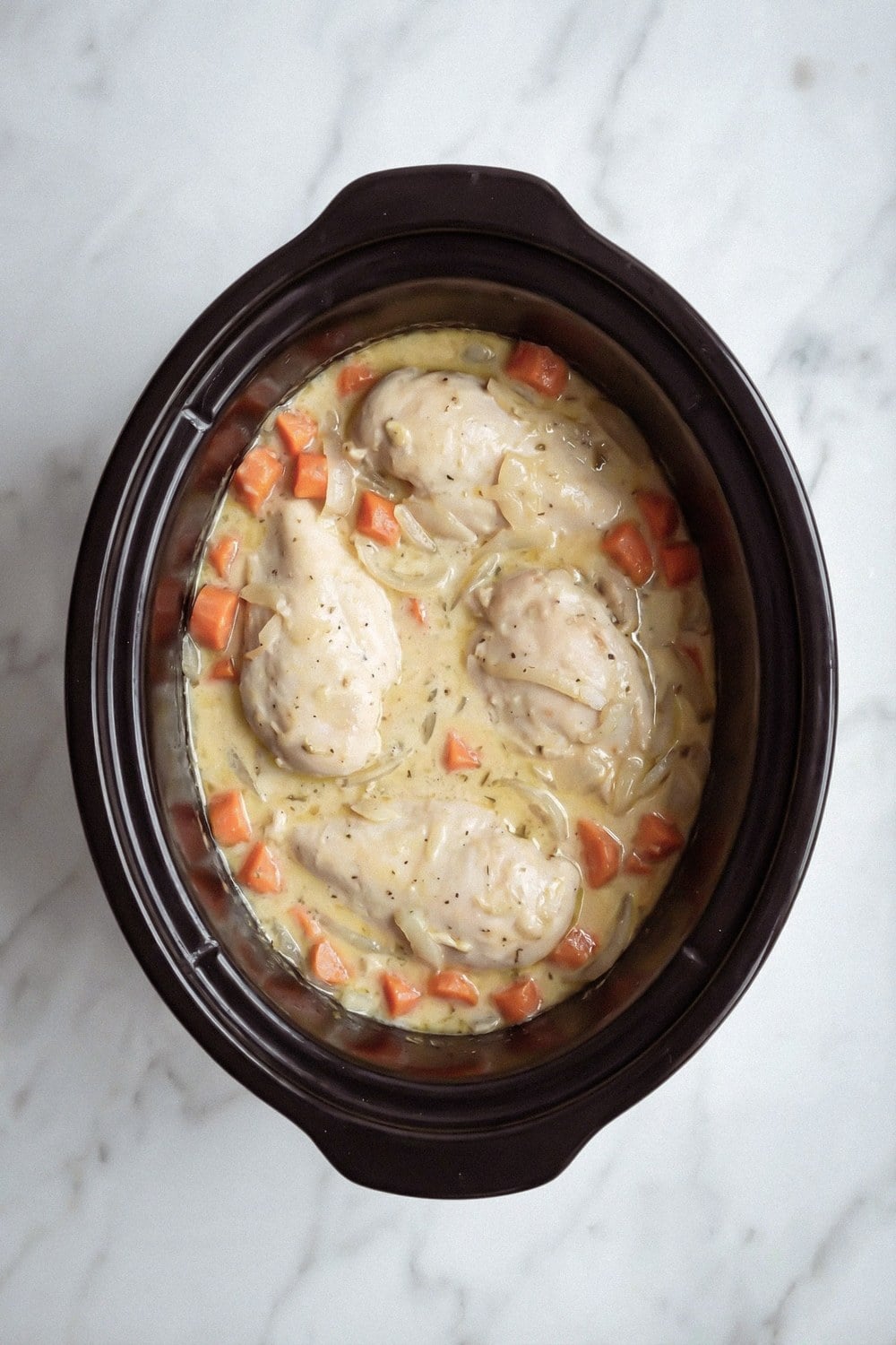Cream sauce poured over chicken and carrots in a slow cooker