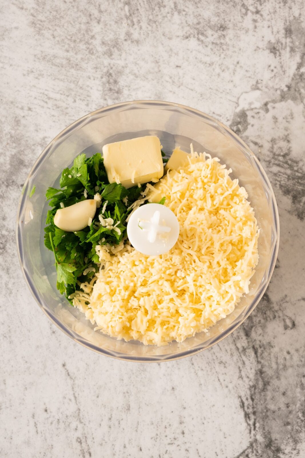 Parsley, butter, garlic, and pecorino romano in a food processor bowl