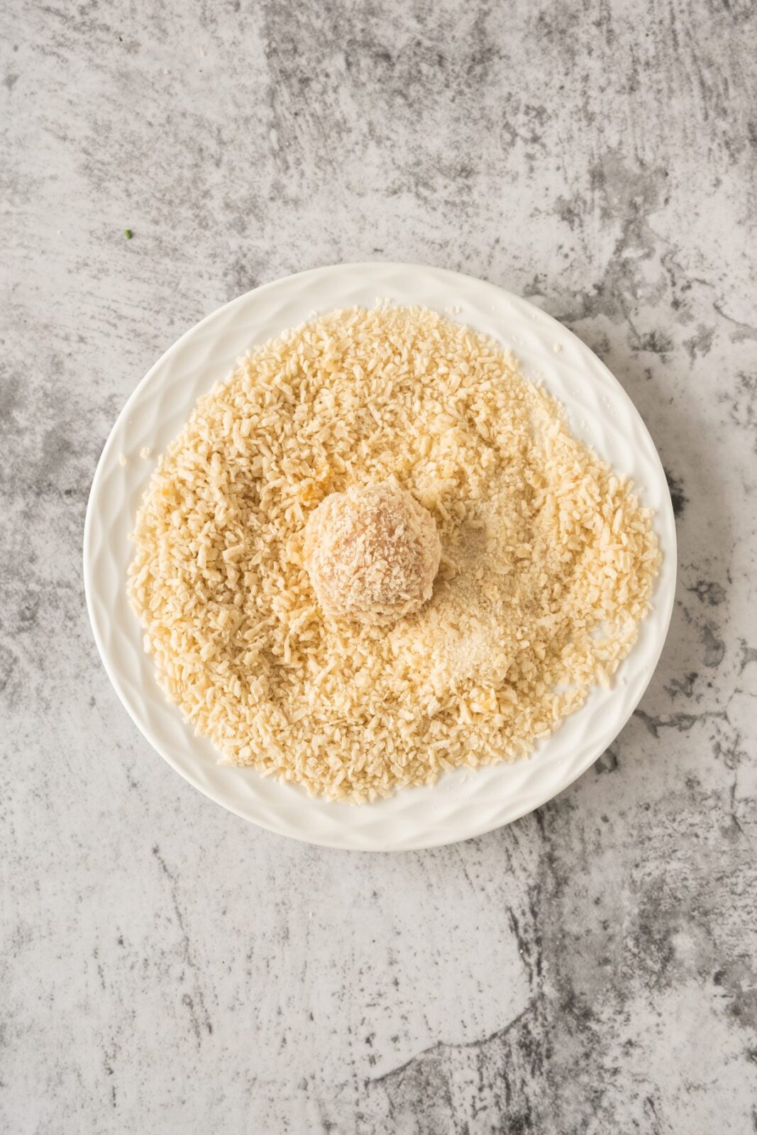 Rolling a chicken ball in panko breadcrumbs on a white plate