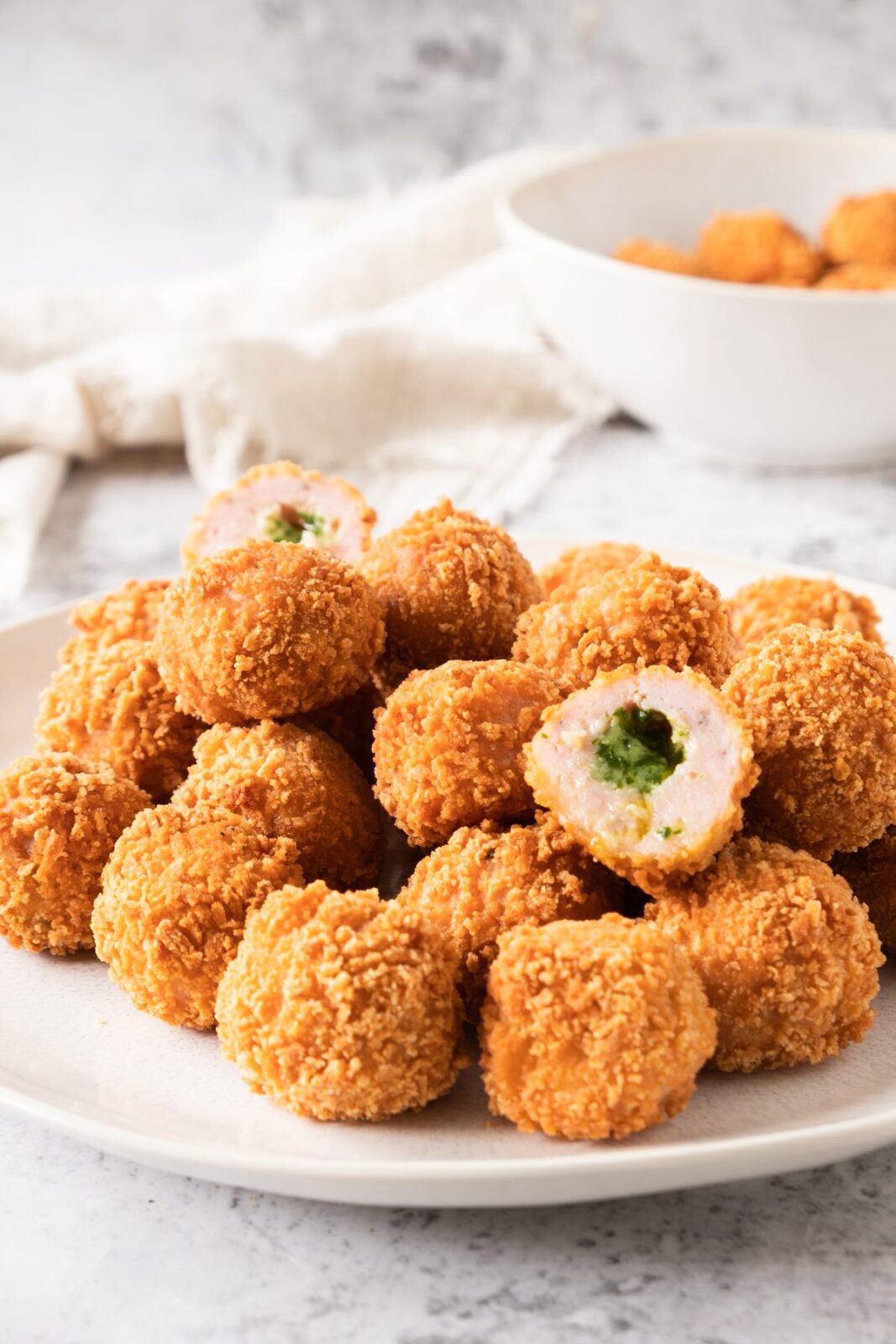 Plate of crispy chicken balls with one cut open to show the herbed butter filling