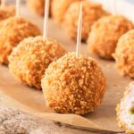Golden fried chicken balls on toothpicks with one cut open showing the green garlic butter filling