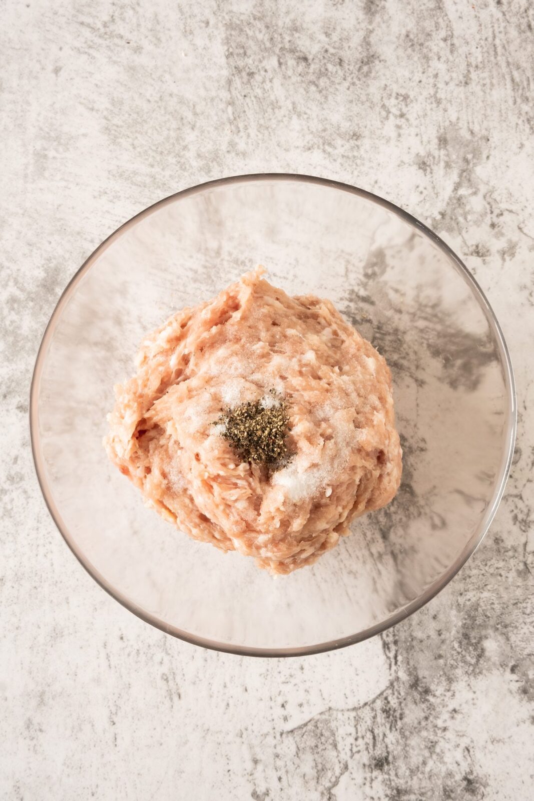 Ground chicken seasoned with salt and pepper in a glass bowl