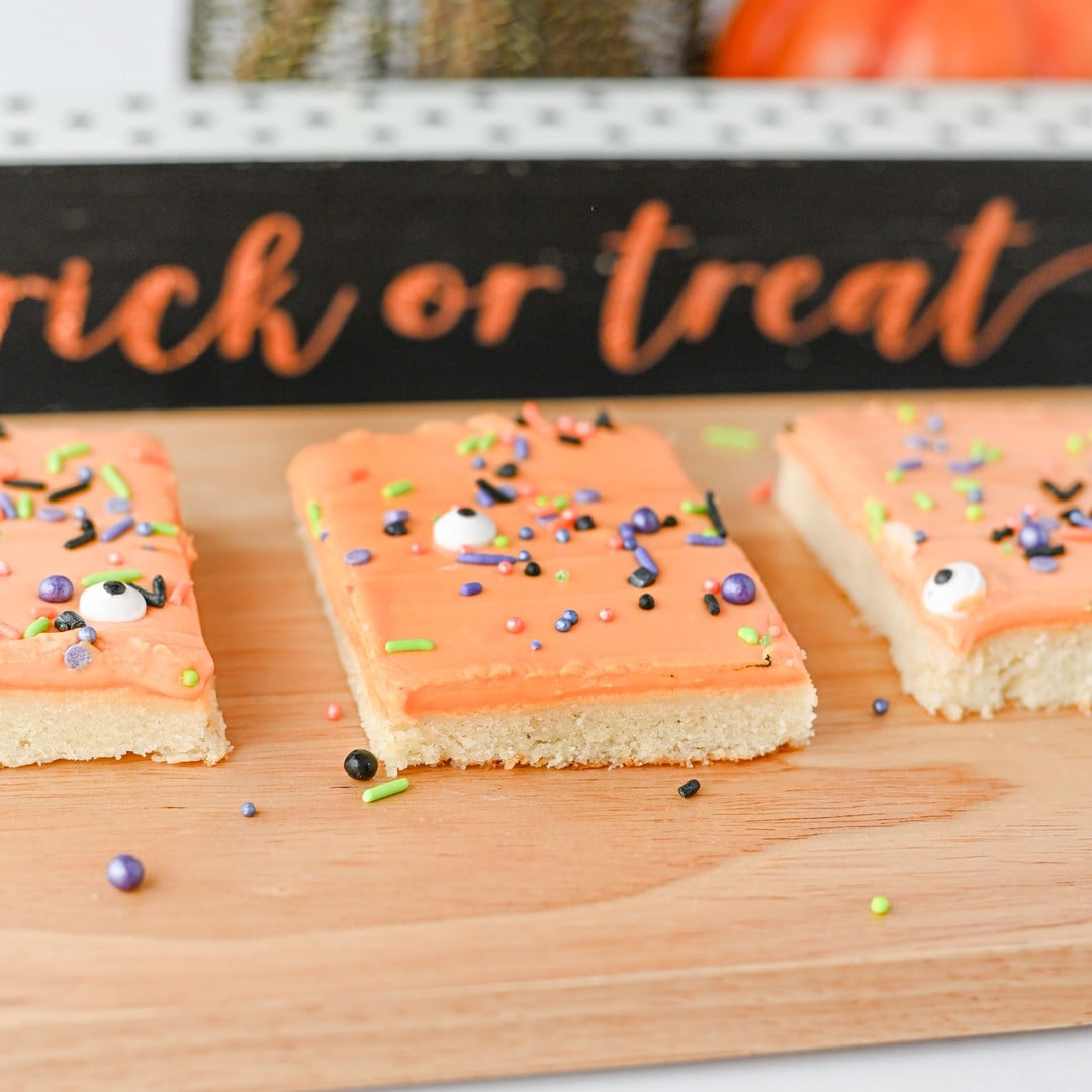 Halloween sugar cookie bars with orange frosting in front of a trick or treat sign