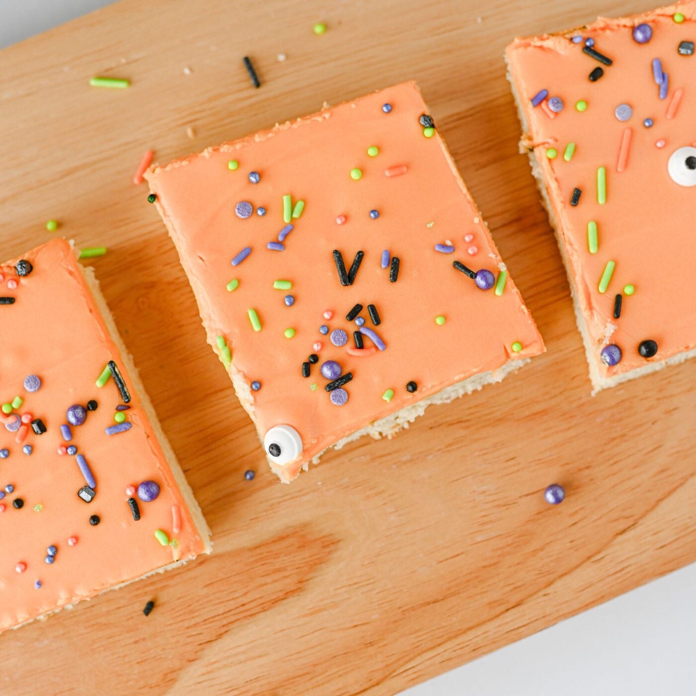 Frosted Halloween sugar cookie bars with sprinkles and candy eyes on a wooden board