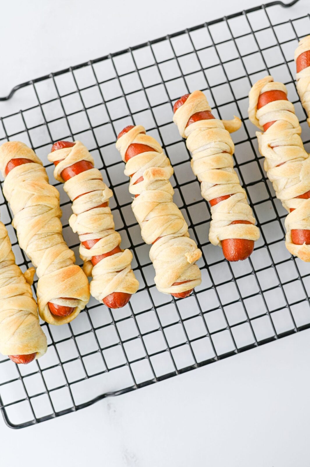 Golden baked mummy hot dogs cooling on a wire rack