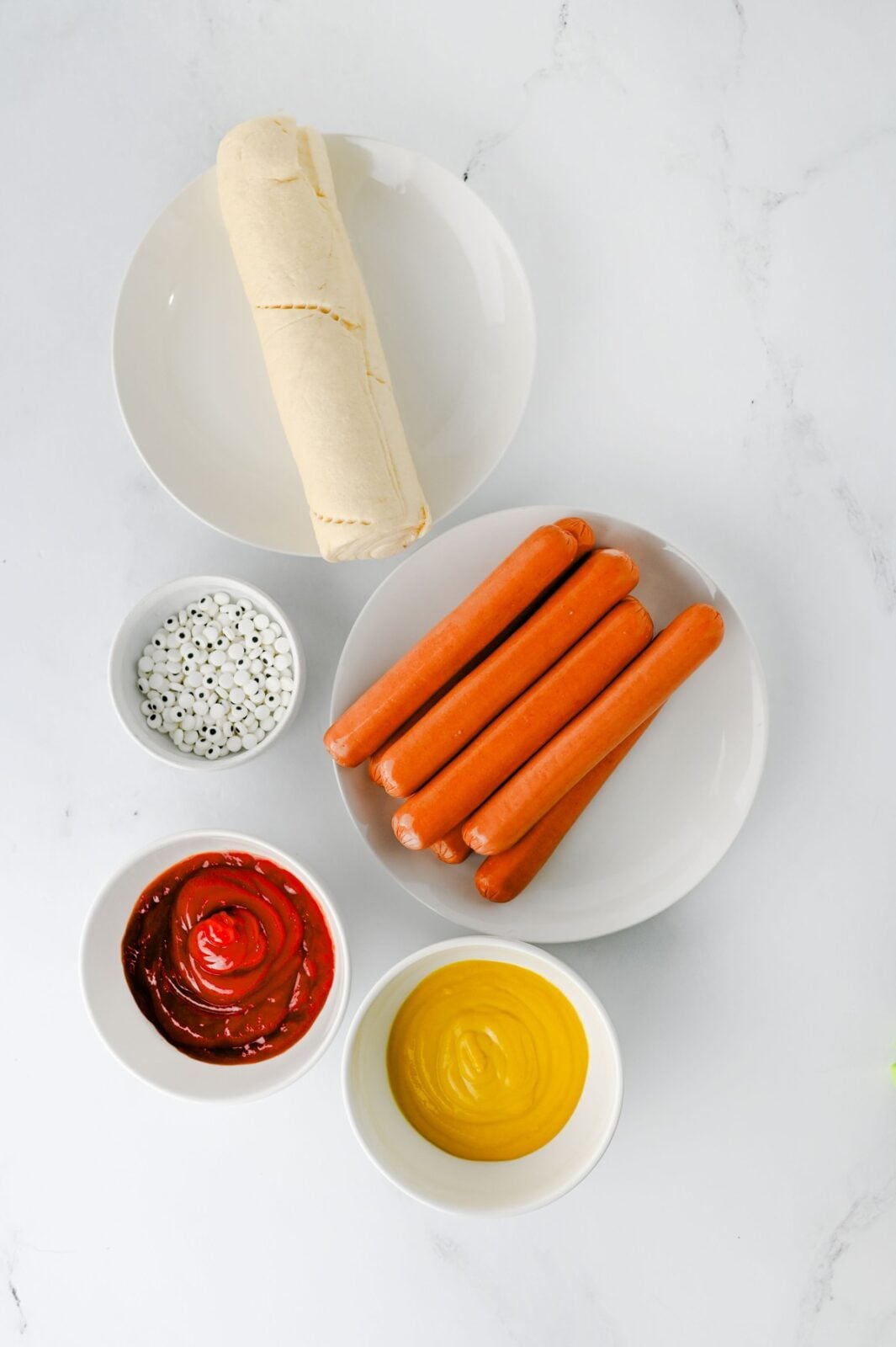 Ingredients for mummy hot dogs: crescent roll dough, hot dogs, candy eyes, ketchup, and mustard
