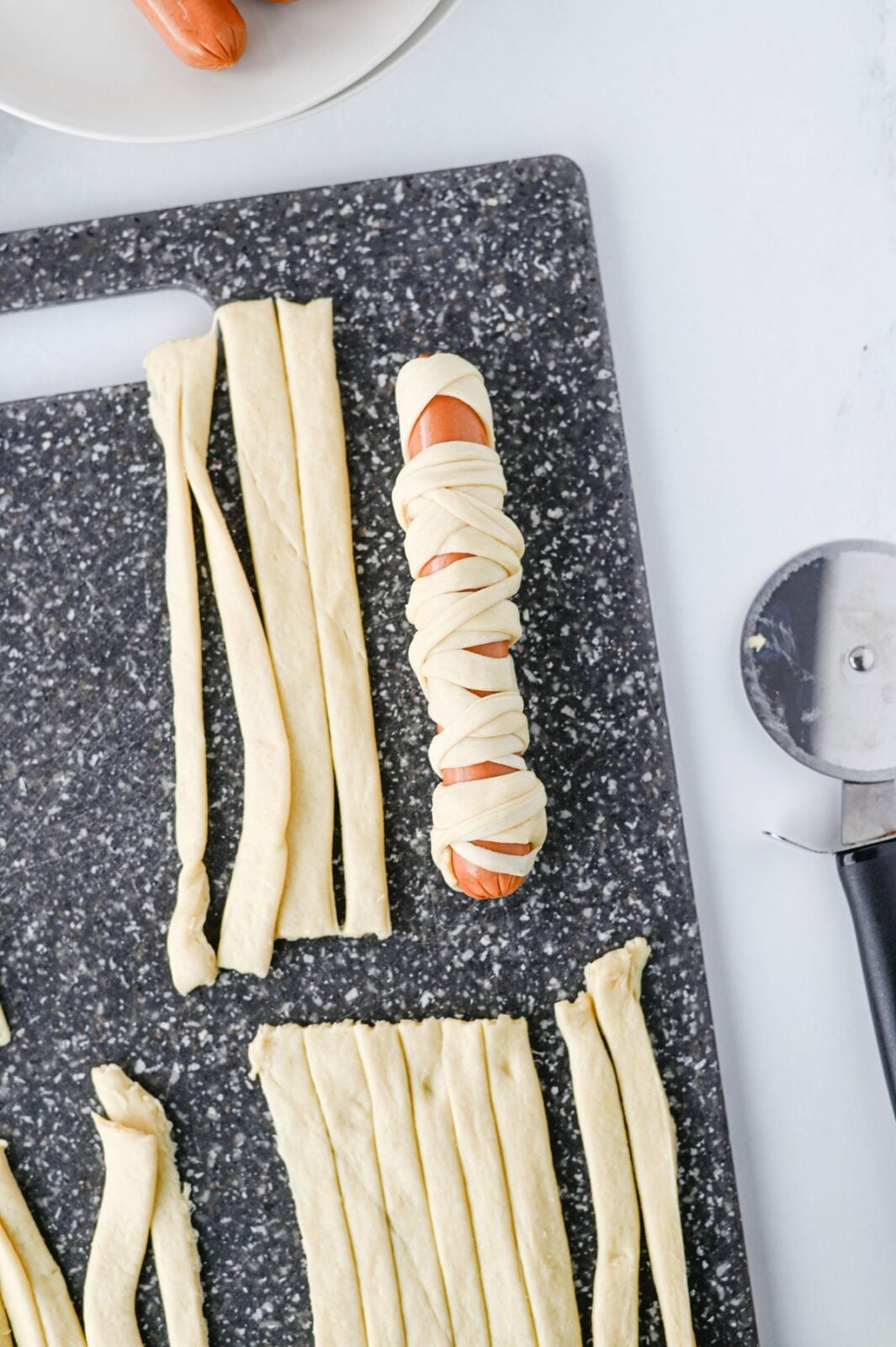 Wrapping strips of crescent dough around a hot dog to make a mummy