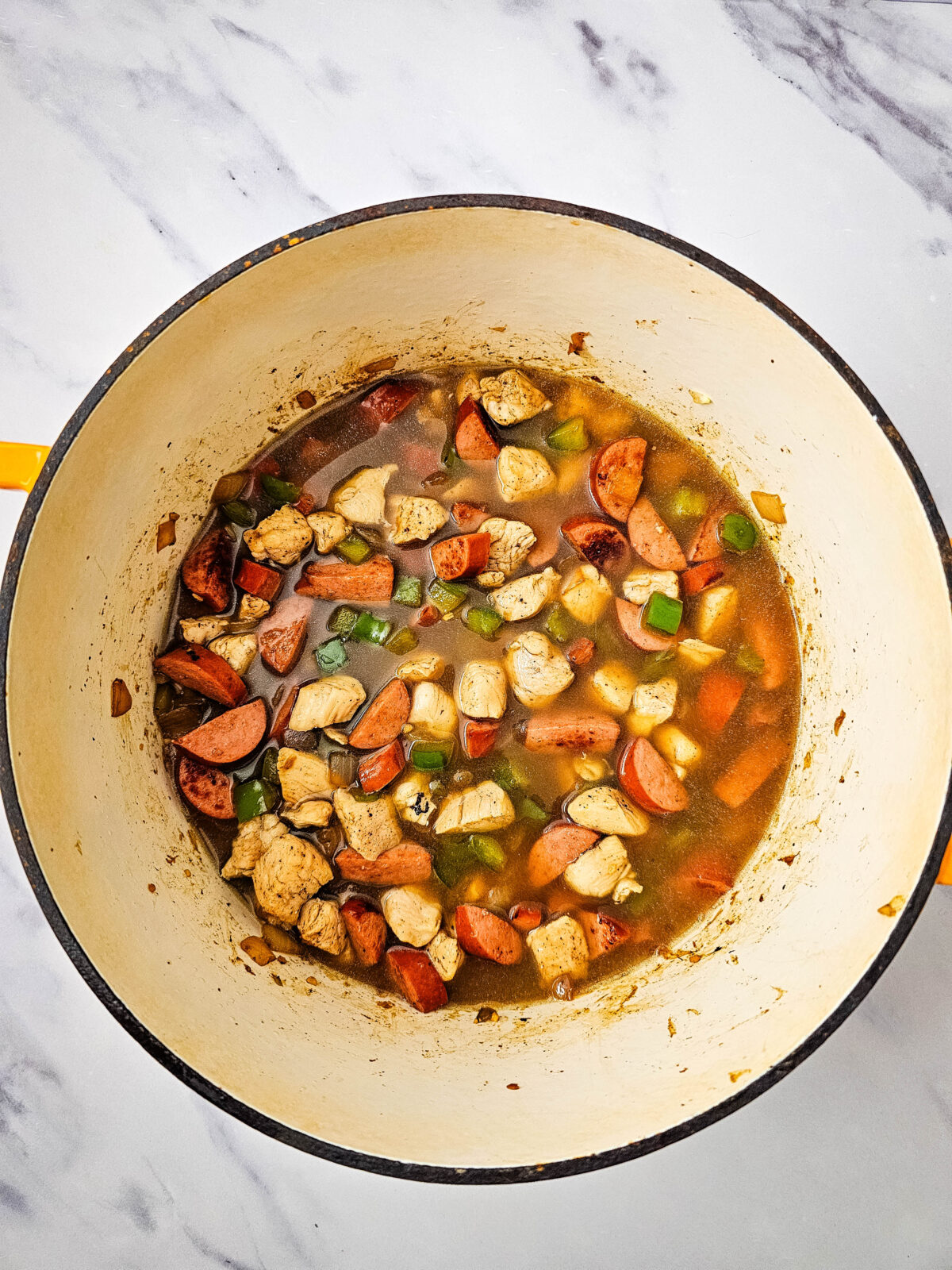 Chicken broth poured over chicken and sausage in a Dutch oven