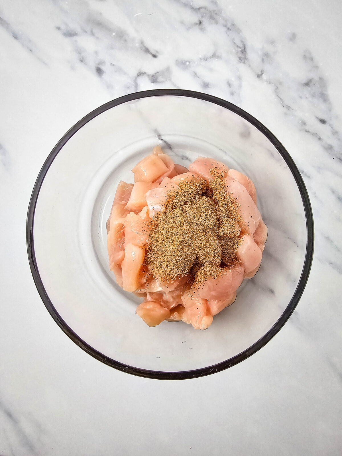 Cubed chicken tossed with Cajun seasoning in a glass bowl