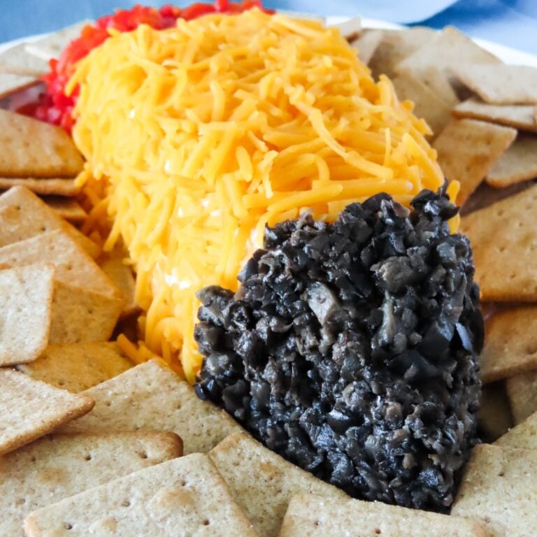 Pencil cheese ball with cheddar body, pimiento eraser, and black olive tip, close up