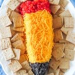Overhead view of a pencil cheese ball appetizer with crackers on a white platter