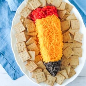 Pencil cheese ball with red pimiento eraser and black olive tip on a cracker platter