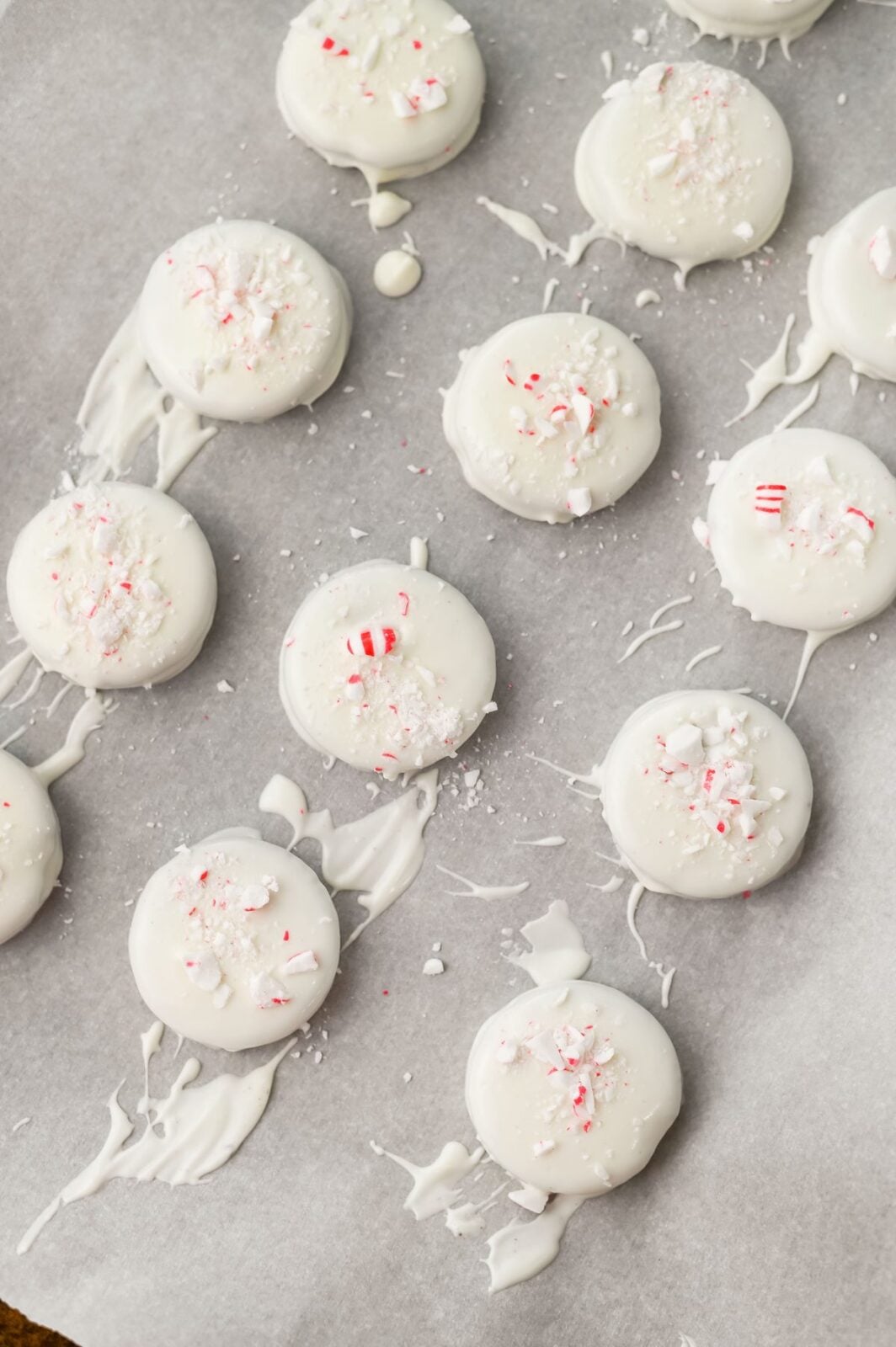 Dipped peppermint crunch Oreos setting on parchment paper with crushed candy canes