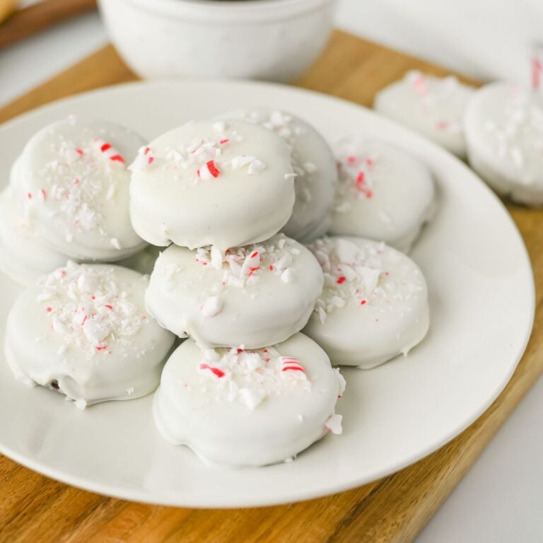 Peppermint crunch Oreos stacked on a white plate topped with crushed candy canes