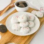 Peppermint crunch Oreos on a white plate with a bowl of Oreo cookies behind