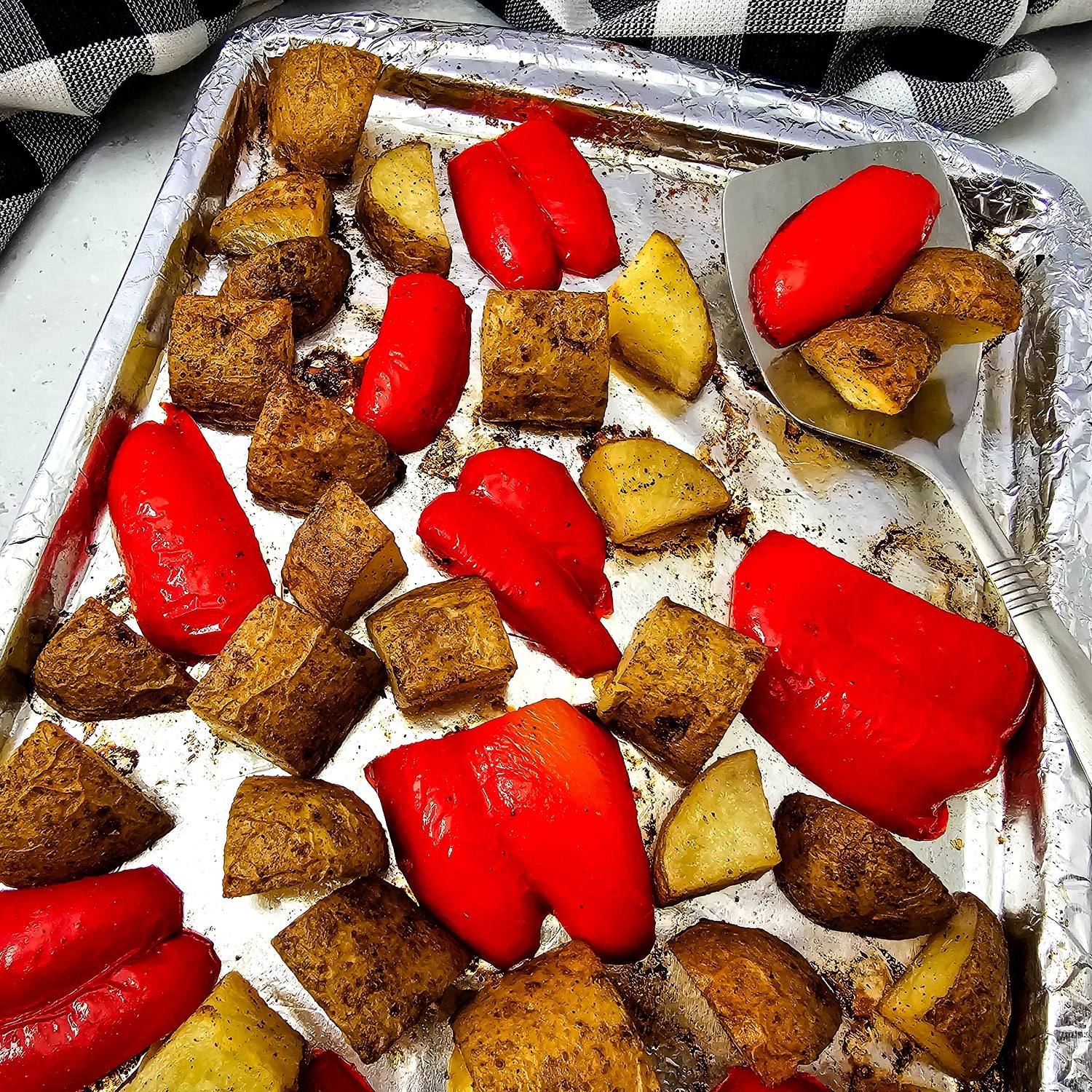 Overhead sheet pan of oven roasted bell peppers and Yukon gold potatoes with a serving spatula