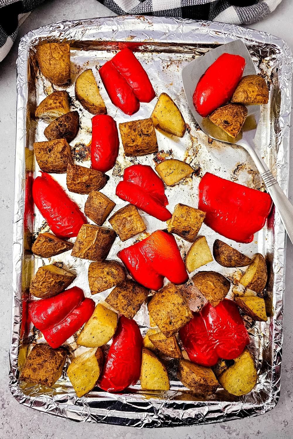 Perfectly roasted bell peppers and potatoes on a sheet pan with a serving spatula