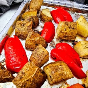 Close-up of roasted red bell peppers and golden potato chunks on a foil-lined sheet pan