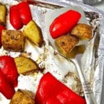 Serving spatula lifting roasted potatoes and red bell peppers from the sheet pan