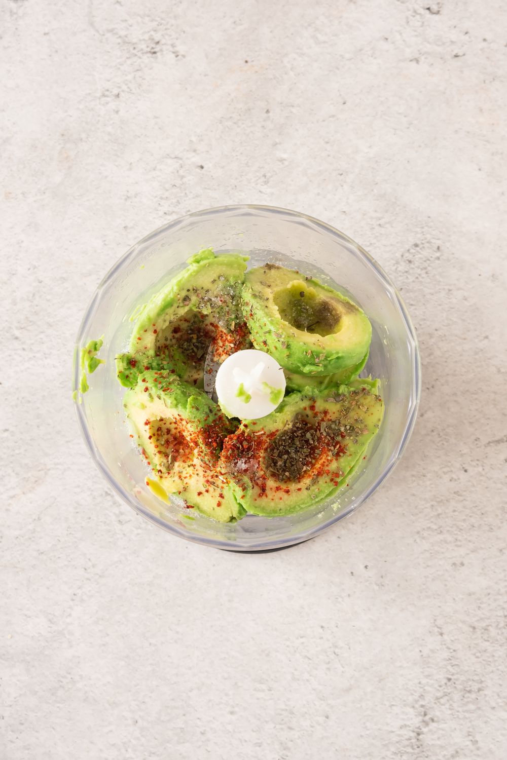 Avocado, lemon juice, and spices in a food processor bowl before blending