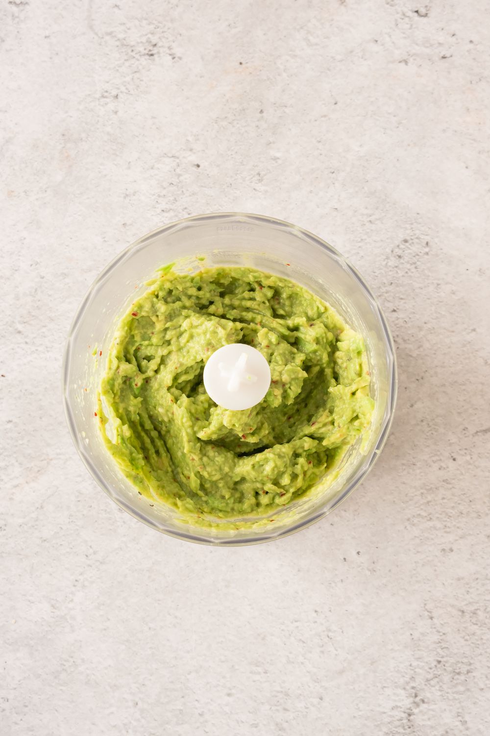 Chunky blended avocado spread in a food processor bowl