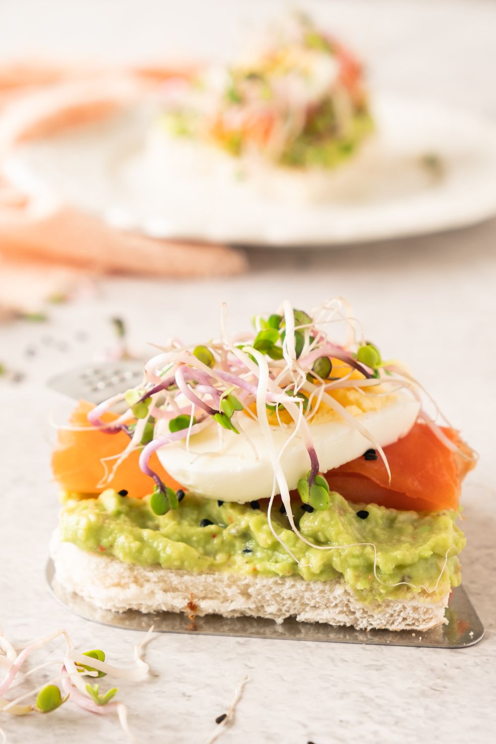 Cross section of a smoked salmon avocado tea sandwich showing the layers of bread, avocado, salmon, and egg