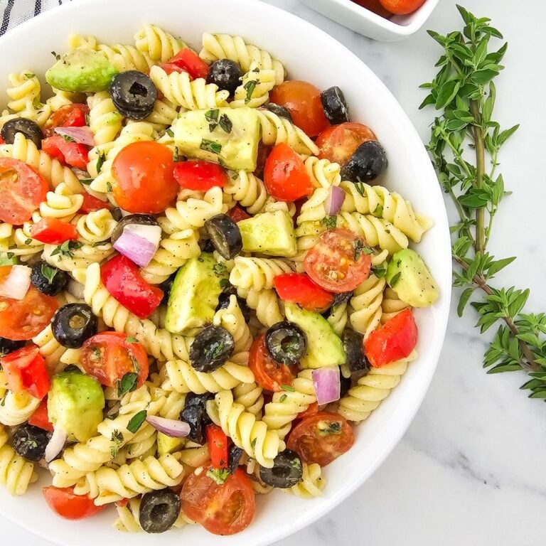 Vegan pasta salad with rotini, cherry tomatoes, black olives, avocado, and red pepper in a white bowl