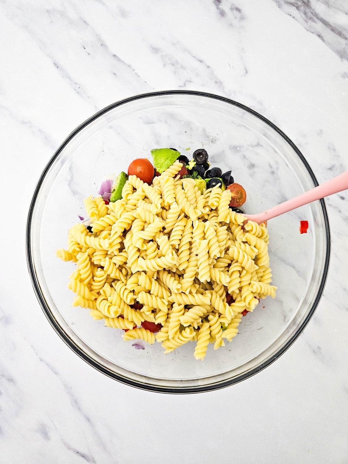 Adding rotini to chopped vegetables to assemble the vegan pasta salad