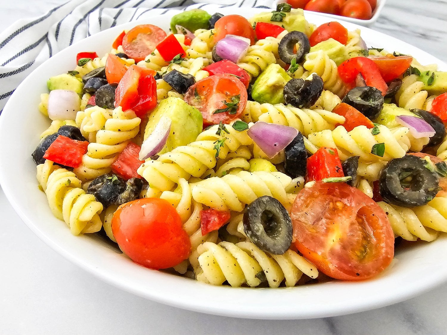 Close-up of vegan pasta salad with cherry tomatoes, black olives, and avocado