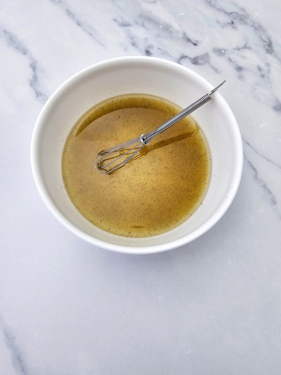 Lemony dressing for vegan pasta salad whisked in a white bowl